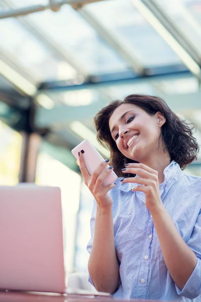 Retrato de una joven juguetona tomando selfie con teléfono móvil mientras está sentada con una computadora portátil en un café al aire libre — Foto de Stock