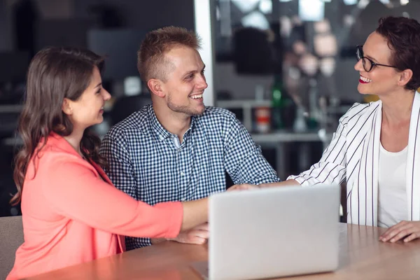 Инвестиционный консультант проводит презентацию для дружелюбной улыбающейся молодой пары, сидящей за своим столом в офисе — стоковое фото
