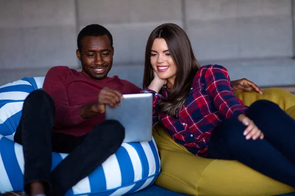 Pareja feliz con la tableta de ordenador y teléfono inteligente en un sofá — Foto de Stock