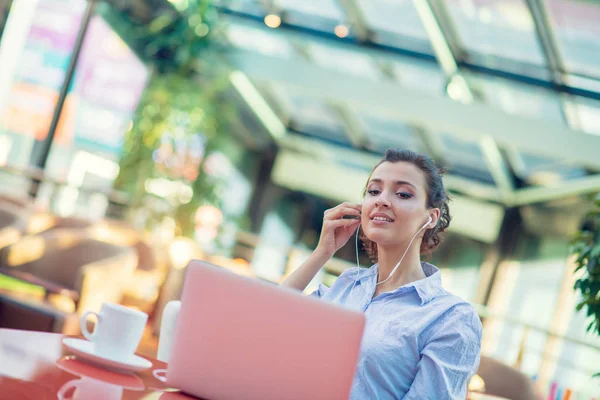 Зображення щасливої жінки, яка використовує ноутбук, сидячи в кафе. Молода жінка сидить у кав'ярні і працює на ноутбуці . — стокове фото