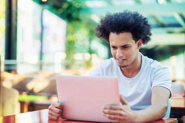 Serious Afro American mężczyzna student w T-shirt siedzi w kawiarni picie kawy na wynos pracy w jego projekt za pomocą laptopa — Zdjęcie stockowe