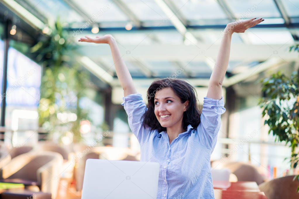 Excited smiling woman celebrating online win, using laptop in cafe, looking at screen, screaming with raising hands.