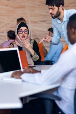 Modern parlak ofis içi beyin fırtınasında toplanan çok ırklı girişim ekibi dizüstü bilgisayar ve tablet bilgisayar üzerinde çalışıyor