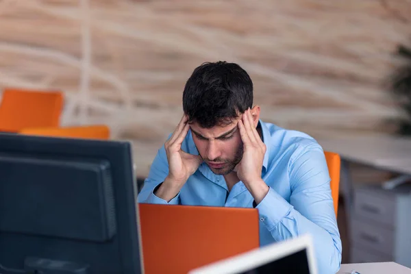 Vista lateral. Jovem empresário barbudo vestindo camisa azul, sentado à mesa e usando laptop. Freelancer verificando e-mail . — Fotografia de Stock