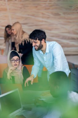 Modern parlak ofis içi beyin fırtınasında toplanan çok ırklı girişim ekibi dizüstü bilgisayar ve tablet bilgisayar üzerinde çalışıyor