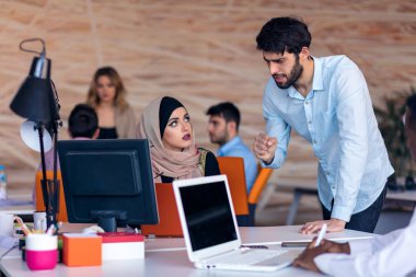 Modern parlak ofis içi beyin fırtınasında toplanan çok ırklı girişim ekibi dizüstü bilgisayar ve tablet bilgisayar üzerinde çalışıyor