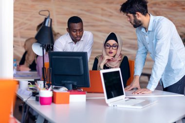 Modern parlak ofis içi beyin fırtınasında toplanan çok ırklı girişim ekibi dizüstü bilgisayar ve tablet bilgisayar üzerinde çalışıyor
