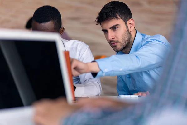 Vista laterale. Giovane uomo d'affari barbuto che indossa camicia blu, seduto a tavola e utilizzando il computer portatile. Email di controllo freelance . — Foto Stock