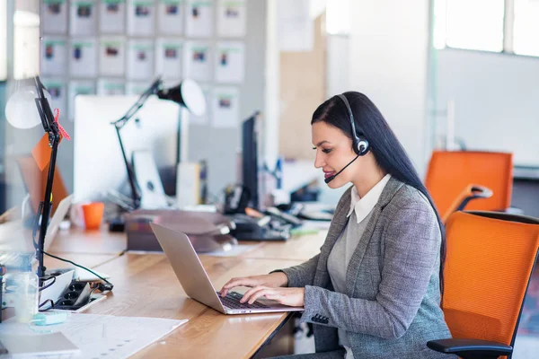Piękny biznesmenów w zestawy słuchawkowe są przy użyciu komputerów i uśmiechając się podczas pracy w biurze. Dziewczyna patrzy na kamery — Zdjęcie stockowe