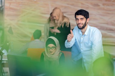 Modern parlak ofis içi beyin fırtınasında toplanan çok ırklı girişim ekibi dizüstü bilgisayar ve tablet bilgisayar üzerinde çalışıyor