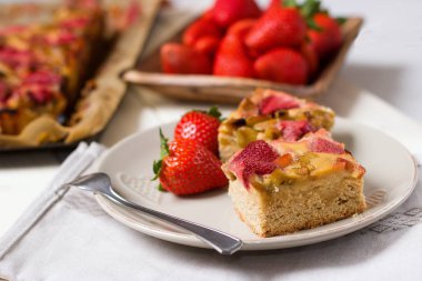 Ahşap kase çilek ve pasta arka planda tüm fırın tepsisi ile güzel plaka üzerinde çilek ve ravent pasta servis