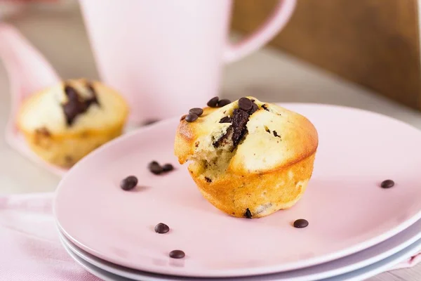 Candid shot of muffin and coffee breakfast. Set and served on pink plate and in pink cup. Muffin is of banana dough and dark chocolate