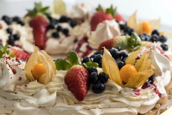 Deliciosa corona de pastel pavlova de merengue francés y crema batida, decorado con fresa, arándanos y physalis — Foto de Stock