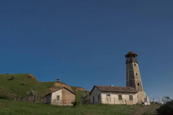 The old lighthouse next to the old houses on the beach at night illuminated by the light of the moon