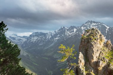 karlı dağ zirveleri altında büyük bir bulut ve ön planda güneş tarafından aydınlatılmış bir taş ile dağ gorge