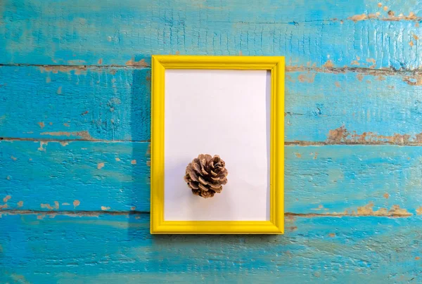 pine cone lies a yellow frame with a white background on a blue textured wooden surface