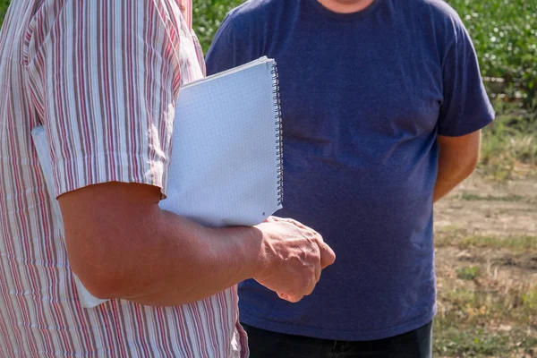 Yaz ziraat mühendisi alanında başka bir kişi ile bir renkli tişörtlü adam elinde bir dizüstü bilgisayar ile bir kalemle yazar anlatılmaktadır