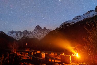 picnic area with burning grill on the background of snowy mountains at night under the starry sky with a meteor in Dombay Karachay-Cherkessia Russia clipart