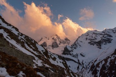mountain peaks covered with snow with bright clouds in the evening at sunset against the blue sky. Kabardino-Balkaria, Russia clipart