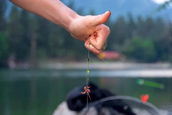 the hands of the fisherman on fishing wear a worm on the hook and hold the feeder with fish food