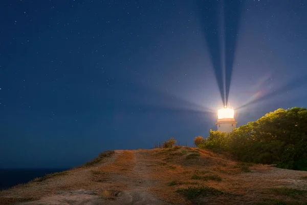 White sea lighthouse in Feodosia, Crimea on the Black Sea with rays of light under the night sky
