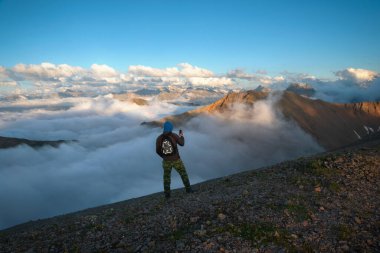 Adam dağın tepesinde, bulutların altında akşam gökyüzünün arka planında.