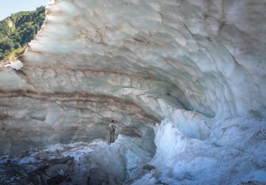 Bir adam dağ buzulunun büyük, karlı bir duvarında duruyor. Alibek Buzulu, 2020