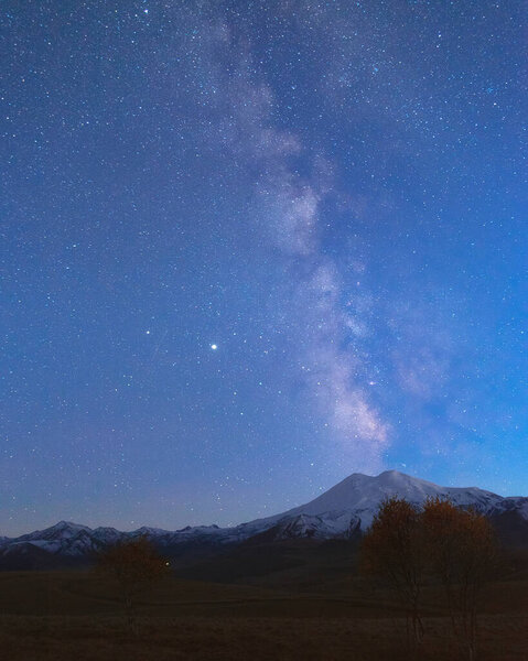 Milky Way in the blue evening sky over the snow-white summit of Mount Elbrus