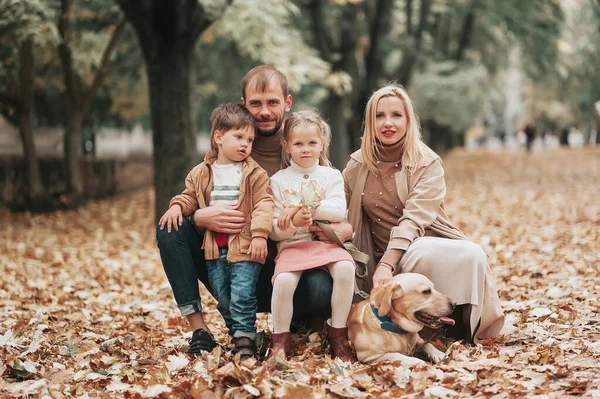 family sitting in autumn park, Mother father son daughter and dog Labrador, fall season