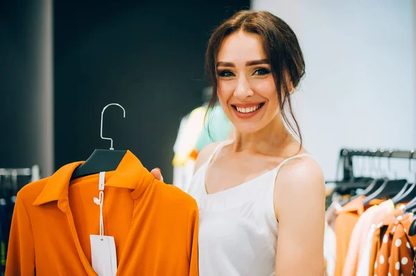 Which one? Beautiful young woman stylist designer trying to choose clothes to herself or customer while working in fashion boutique. Fashion stylist show new collection and trends in store