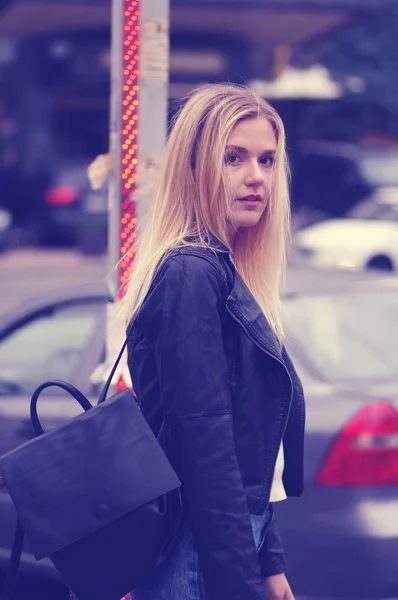 Menina loira bonita posando ao ar livre. A menina está vestida com uma jaqueta de couro preto e uma camisola branca . — Fotografia de Stock