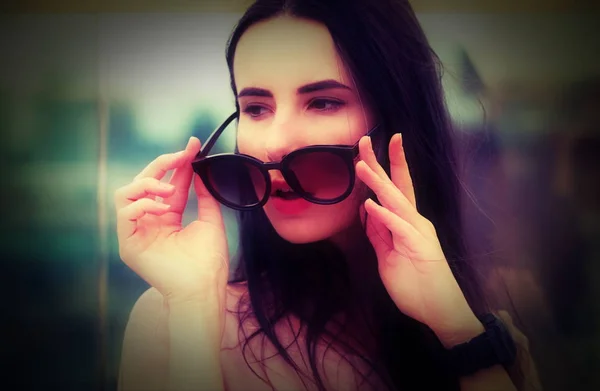Een langharige jonge brunette vrouw speelt met zonnebril. — Stockfoto