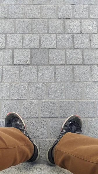 Ноги сидящего человека в потрепанных брюках и кроссовках — стоковое фото