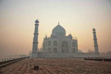Agra, India. White marble Taj Mahal complex with minarets and walls through the haze and smog from Agra Fort fortress UNESCO heritage behind Yamuna river in Agra, India