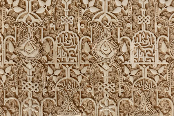 The detailed and intricate geometric patterns and Islamic calligraphy of a wall carving at the famous Alhambra palace- fortress in Granada, Spain europe