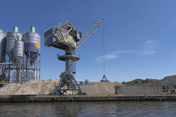 Kargo gemisinden kum, yol metali ve çakıl boşaltan vinç, ağır araç ve portal vinç yükleyicisi liman terminalinde ağır malzemelerle çalışıyor.