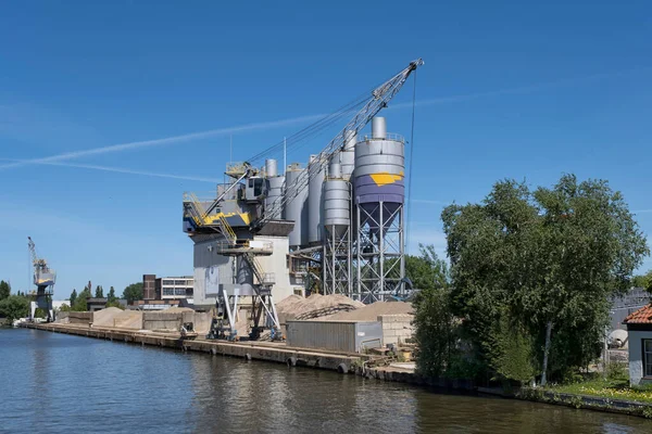 Bulk-handling crane unloading sand, road metal and gravel from cargo vessel ship, heavy vehicle and portal crane loader working with bulk materials in dock terminal