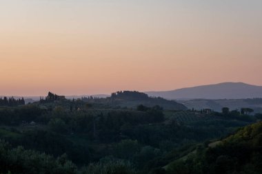 Toskana, Girit Senesi topraklarında kırsal alan. Yuvarlanan tepeler, taşra çiftliği, selvi ağaçları, sıcak günbatımında yeşil alan. Siena, İtalya, Avrupa