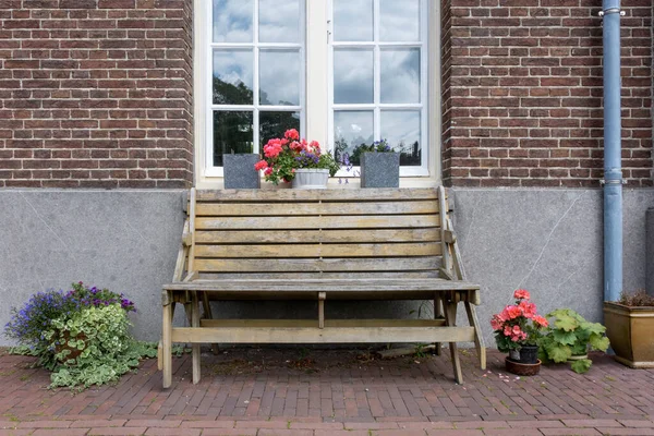 房子前面的木制长椅的前视图 窗上有花的倒影 — 图库照片