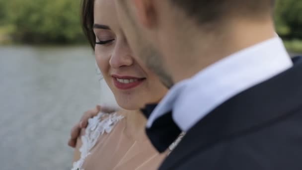 Beautiful wedding couple. Elegant gentle stylish groom and bride near river or lake. Newlywed couple in love. Bride lokking at camera Stock Footage