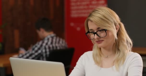 Mujer rubia con estilo que trabaja en la oficina. Caucásico chica páginas de desplazamiento, la lectura de noticias en Internet utilizando su ordenador portátil. Concepto de trabajo en equipo — Vídeos de Stock