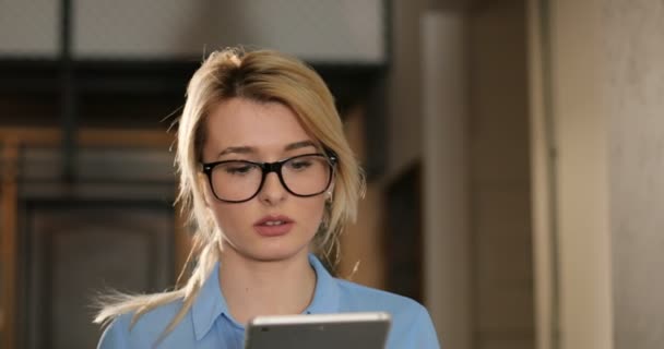 Mujer joven guapo usando tableta PC caminando a través de la oficina, área de coworking. .. Cierra la celda de la mujer de negocios hablando por teléfono en la oficina, en el interior. Retrato plano — Vídeo de stock