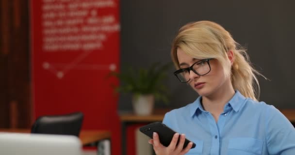 Mulher atraente em óculos usando telefone inteligente no escritório. Feche o telemóvel de uma mulher de negócios a falar ao telefone no escritório, dentro de casa. Um tiro de perto. Retrato tirado — Vídeo de Stock