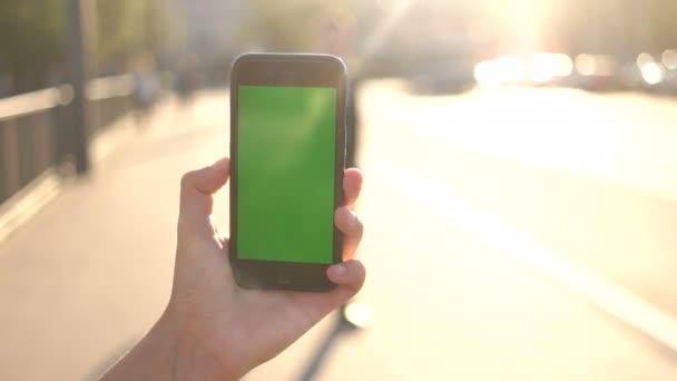 Man handen met slimme telefoon met groen scherm op de achtergrond van de stad tijdens de zonsondergang. — Stockvideo