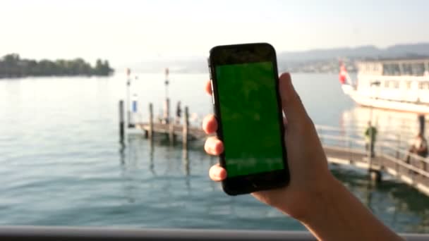 Крупный план человека руки держа смартфон с зеленым экраном на морском фоне на причале. Ключ хрома . — стоковое видео