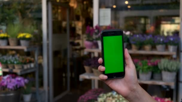 Mãos de homem segurando telefone inteligente com tela verde no fundo da loja de flores. Chave Chroma . — Vídeo de Stock