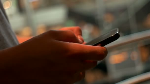 Primer plano de hombre joven utilizando el teléfono inteligente para charlar con amigos en el fondo del centro comercial por la noche  . — Vídeo de stock