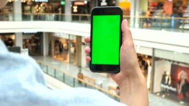Genç erkek alışveriş merkezi zemin üzerine yeşil ekranlı akıllı telefon kullanarak. Chroma anahtar.