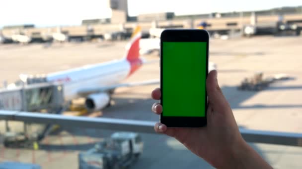 Nahaufnahme von Menschenhänden, die das Smartphone mit grünem Bildschirm auf dem Flugzeugparkplatz halten. Chroma-Schlüssel. Green Screen. — Stockvideo