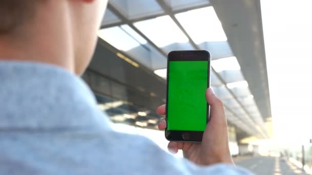 Close up shot of man hands holding the smart phone with green screen on airport background. View from the back. Chroma key. — Stock Video